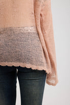 Close up of scallop hem detail on sheer dusty pink oversized open knit jumper with deer graphic, worn by model