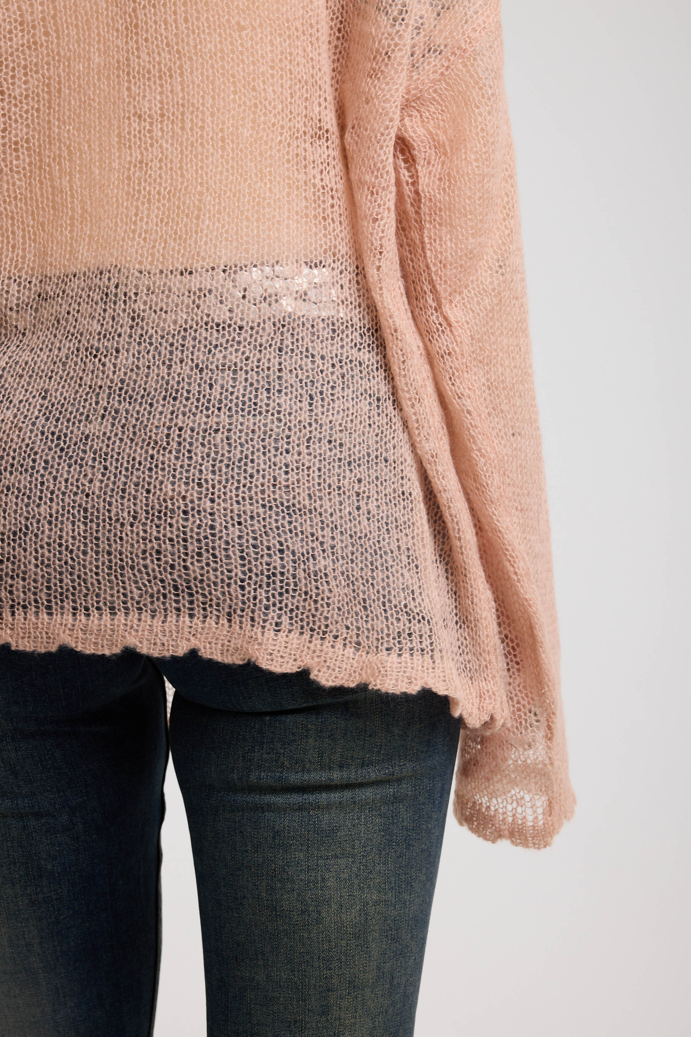 Close up of scallop hem detail on sheer dusty pink oversized open knit jumper with deer graphic, worn by model