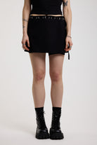 Black eyelet detail mini wrap skirt with adjustable ties, worn by model