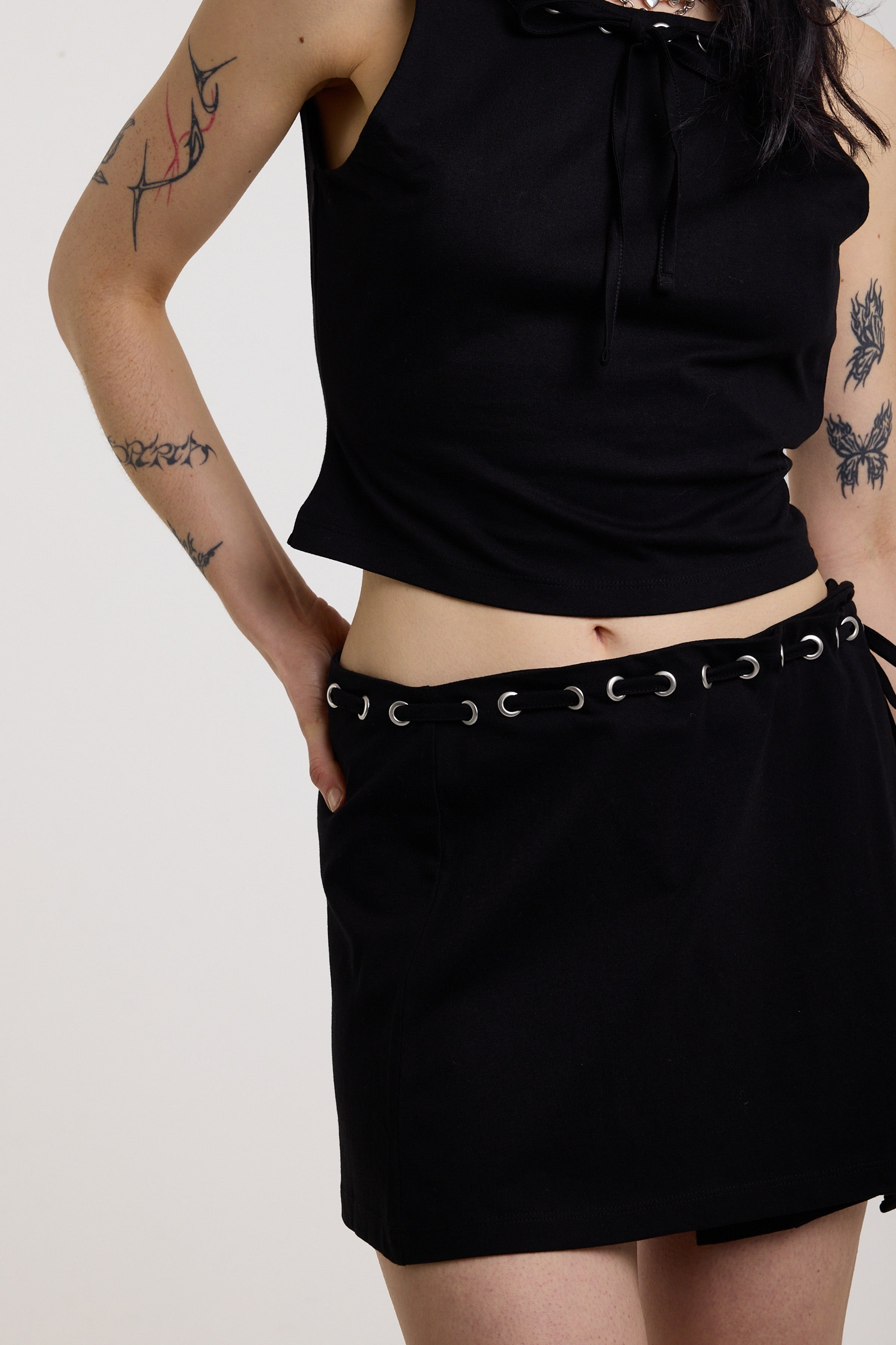Black eyelet detail mini wrap skirt with adjustable ties, worn by model