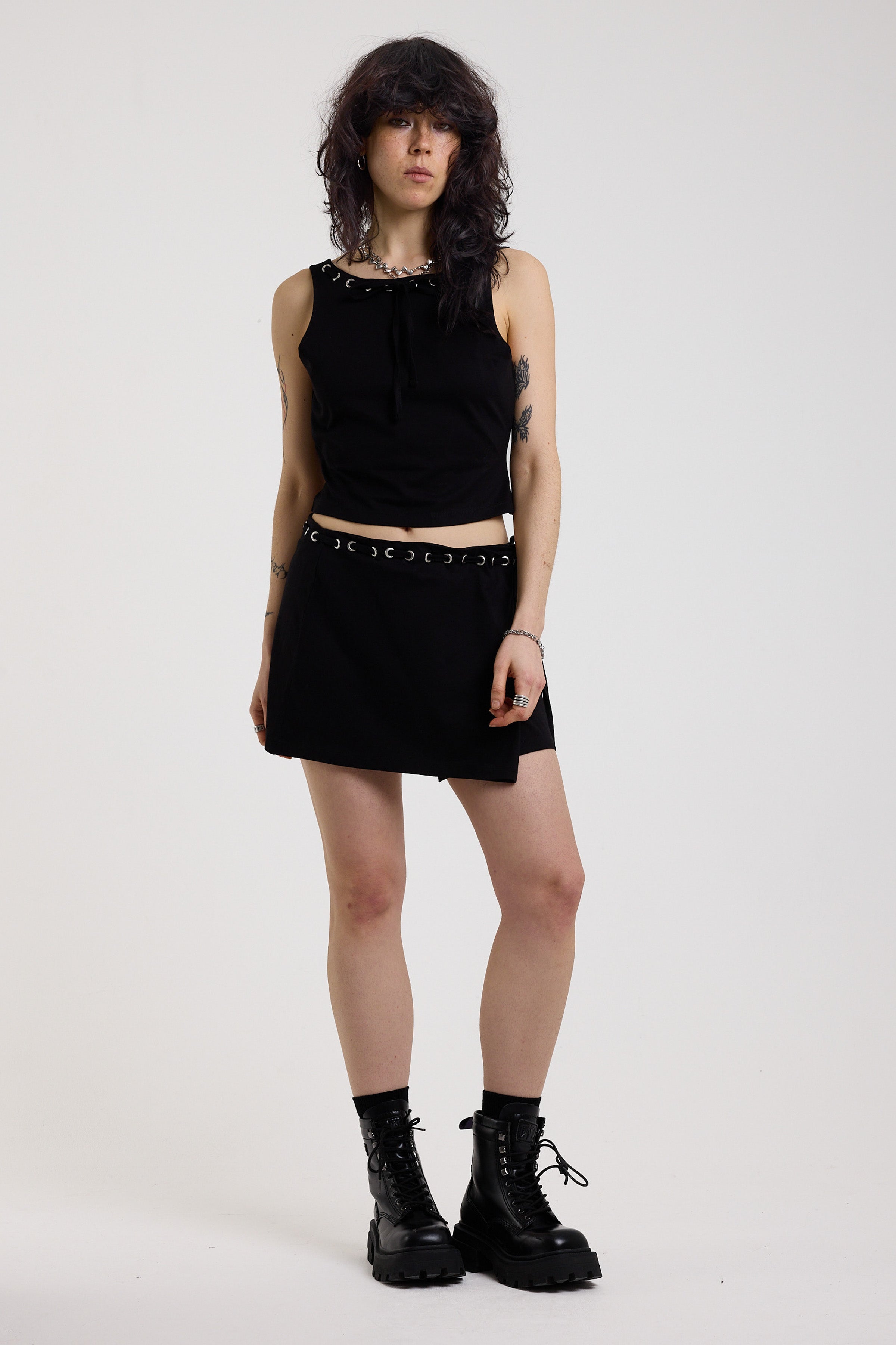 Black slash neck open back tank top with silver eyelet detail, worn by model
