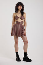 Grunge burgundy check strappy mini dress with cut out panels, silver hardware and tie back detail, worn by model