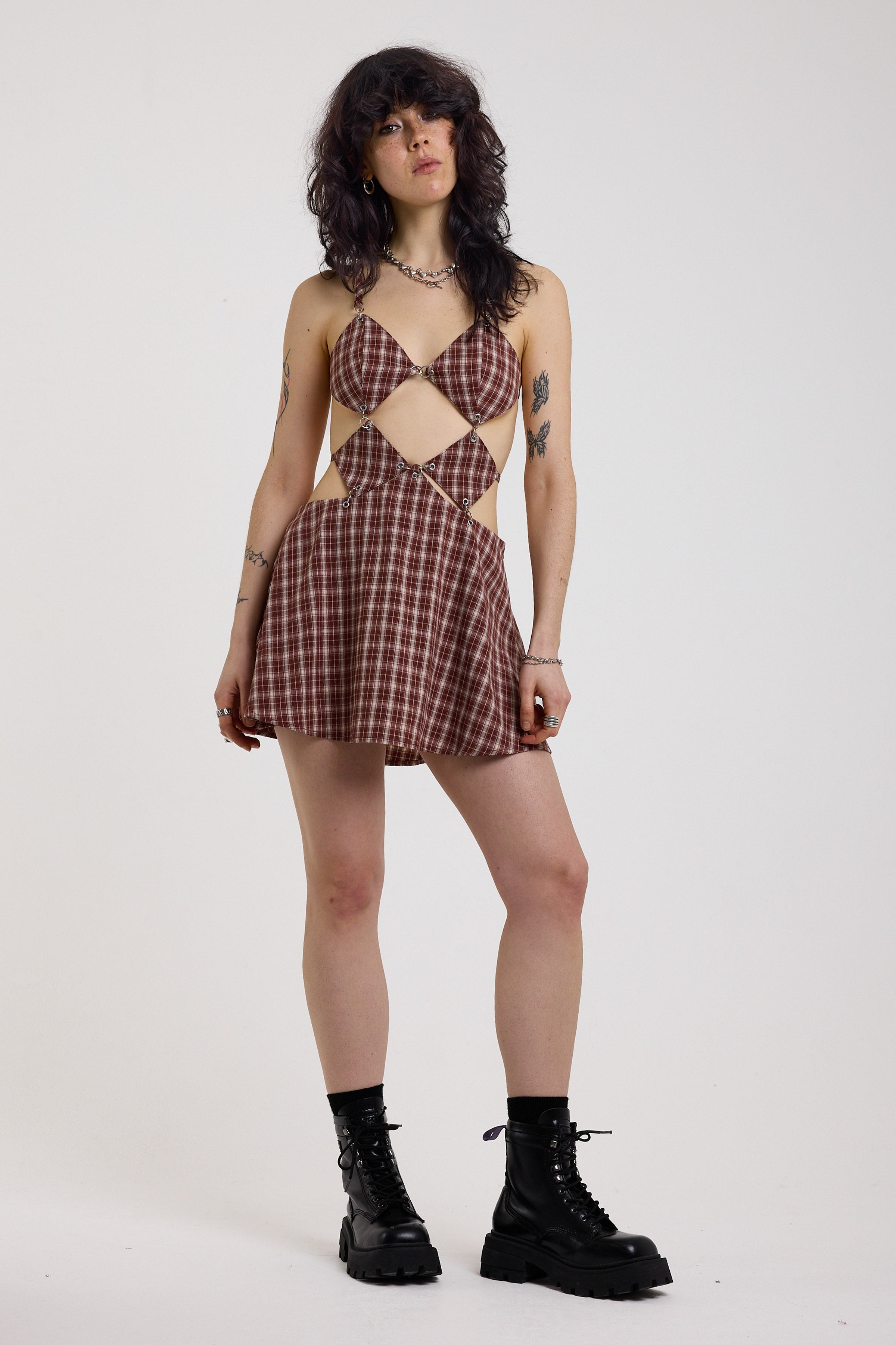 Grunge burgundy check strappy mini dress with cut out panels, silver hardware and tie back detail, worn by model