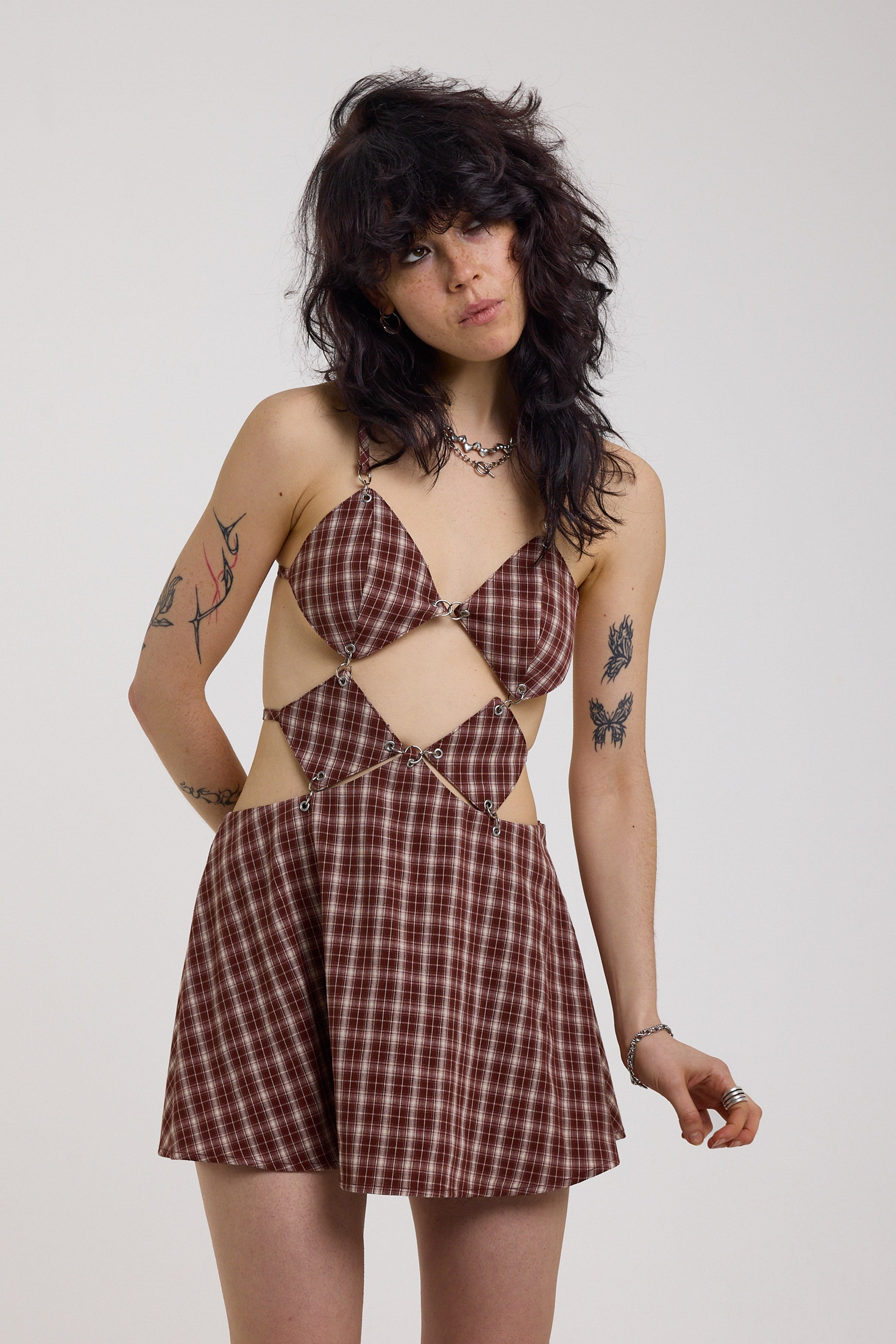 Grunge burgundy check strappy mini dress with cut out panels, silver hardware and tie back detail, worn by model