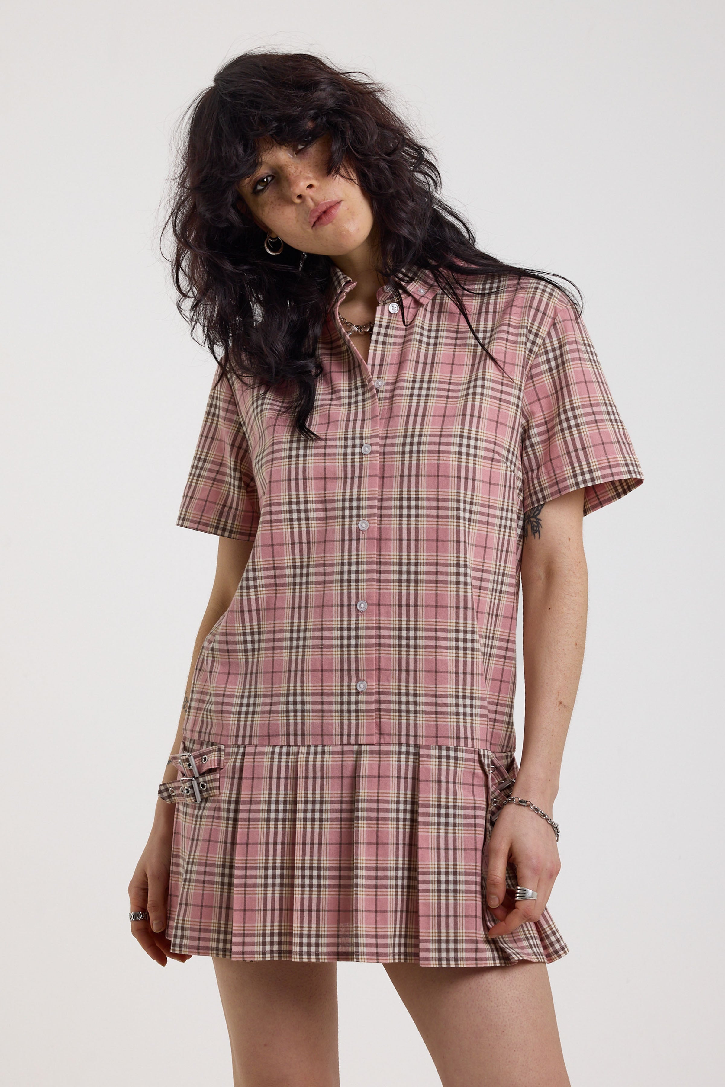 Pink tartan check mini dress with pleated mini skirt buttons, collar and silver buckle detail, worn by model