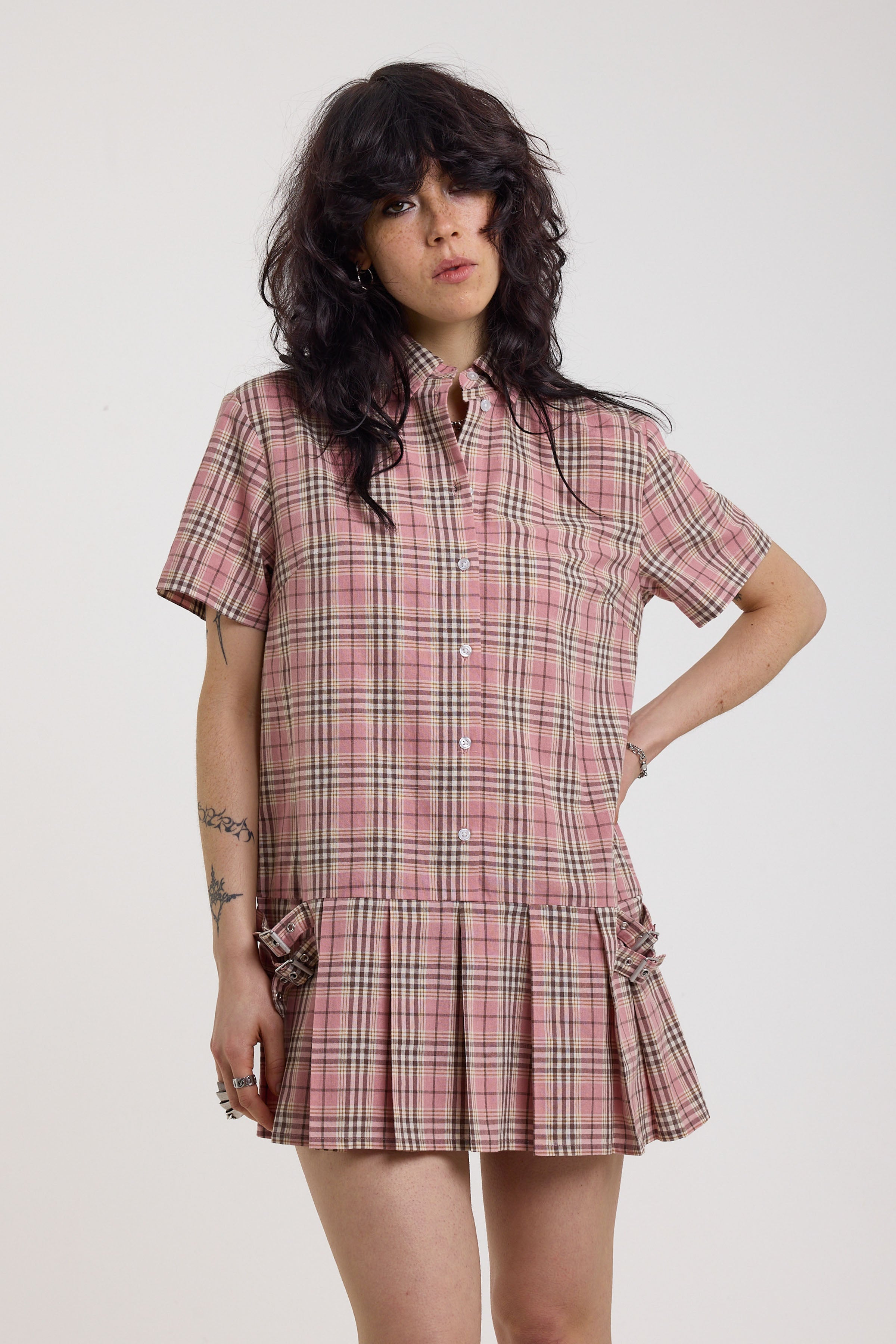 Pink tartan check mini dress with pleated mini skirt buttons, collar and silver buckle detail, worn by model
