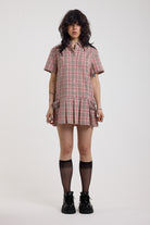 Pink tartan check mini dress with pleated mini skirt buttons, collar and silver buckle detail, worn by model