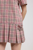 Close up of silver buckles and pleated mini skirt on pink tartan check mini dress, worn by model