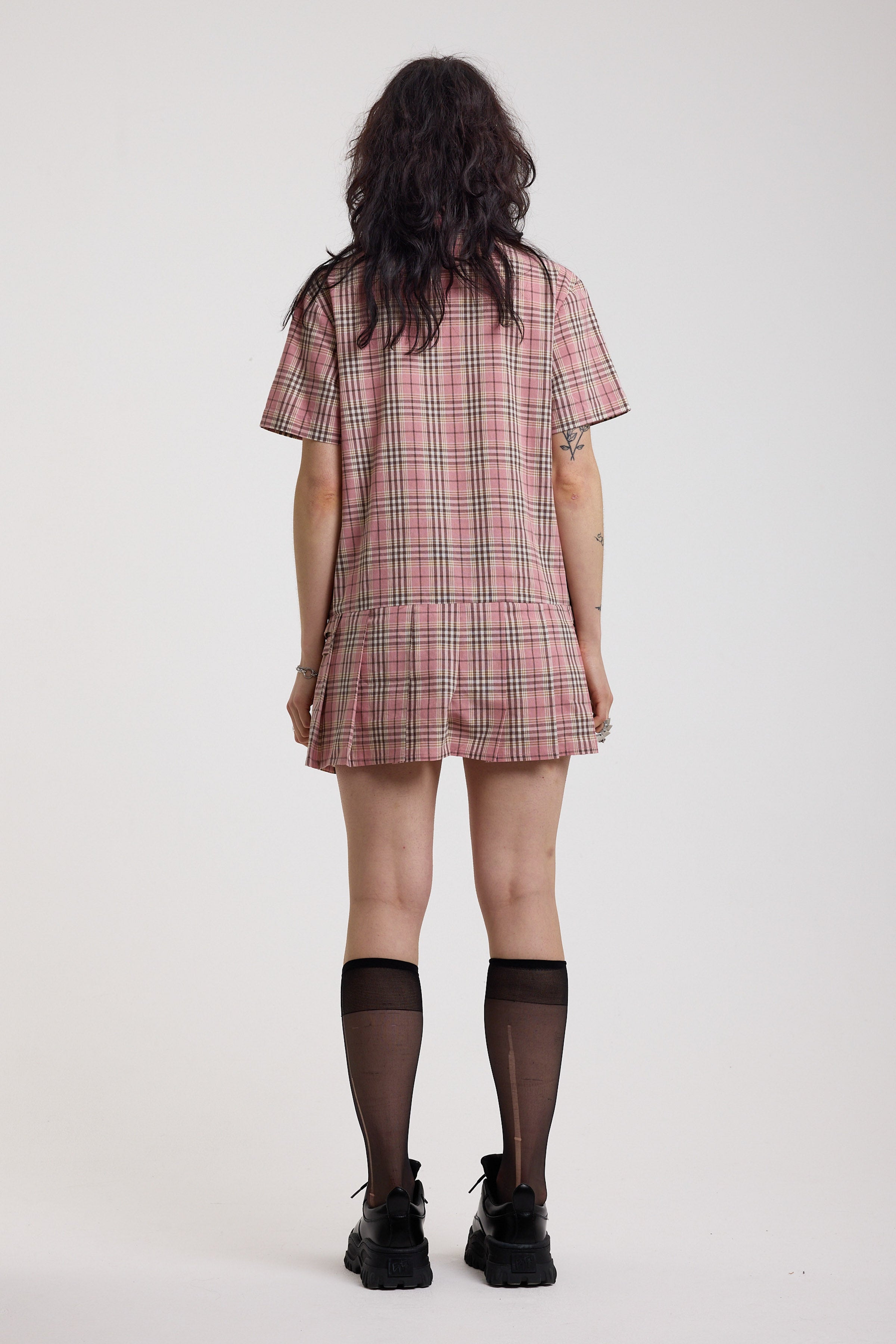 Back of pink tartan check mini dress with pleated mini skirt buttons, collar and silver buckle detail, worn by model