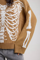 Close up showing skeleton graphic on brown oversized knit jumper, worn by model
