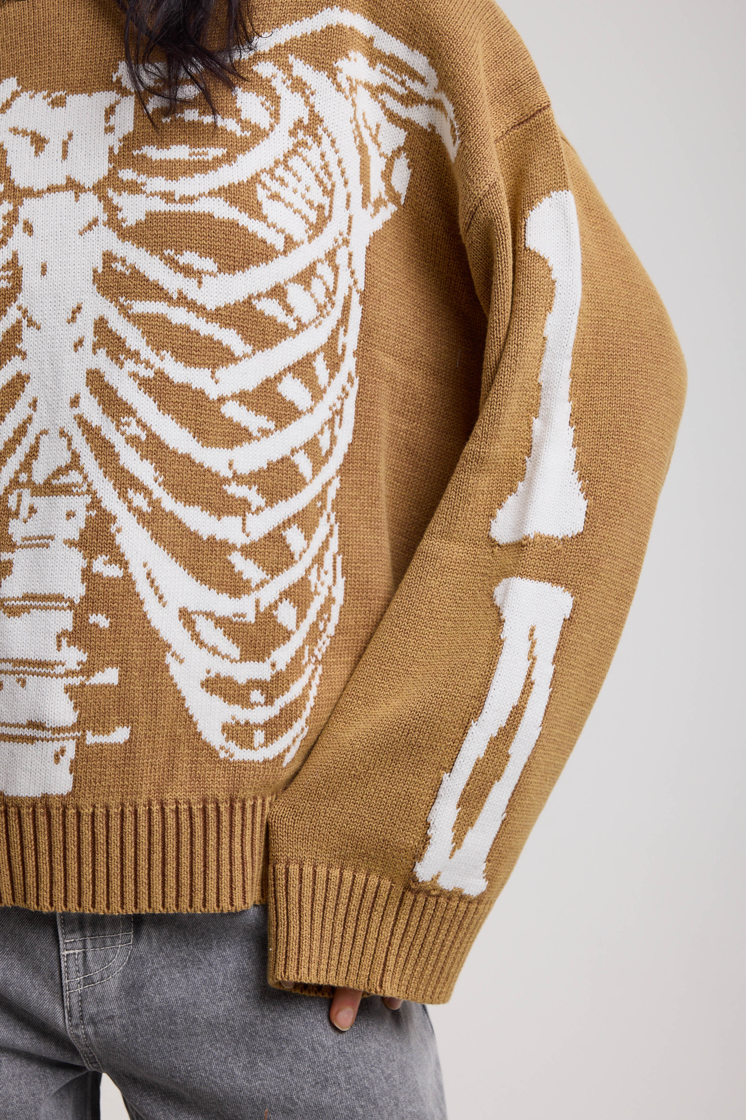 Close up showing skeleton graphic on brown oversized knit jumper, worn by model