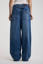 Back view of dark blue ultra baggy wide leg jeans with hardware eyelet detail cinch back belt, worn by model