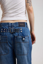 Close up showing hardware eyelet detail cinch back belt on dark blue ultra baggy wide leg jeans, worn by model