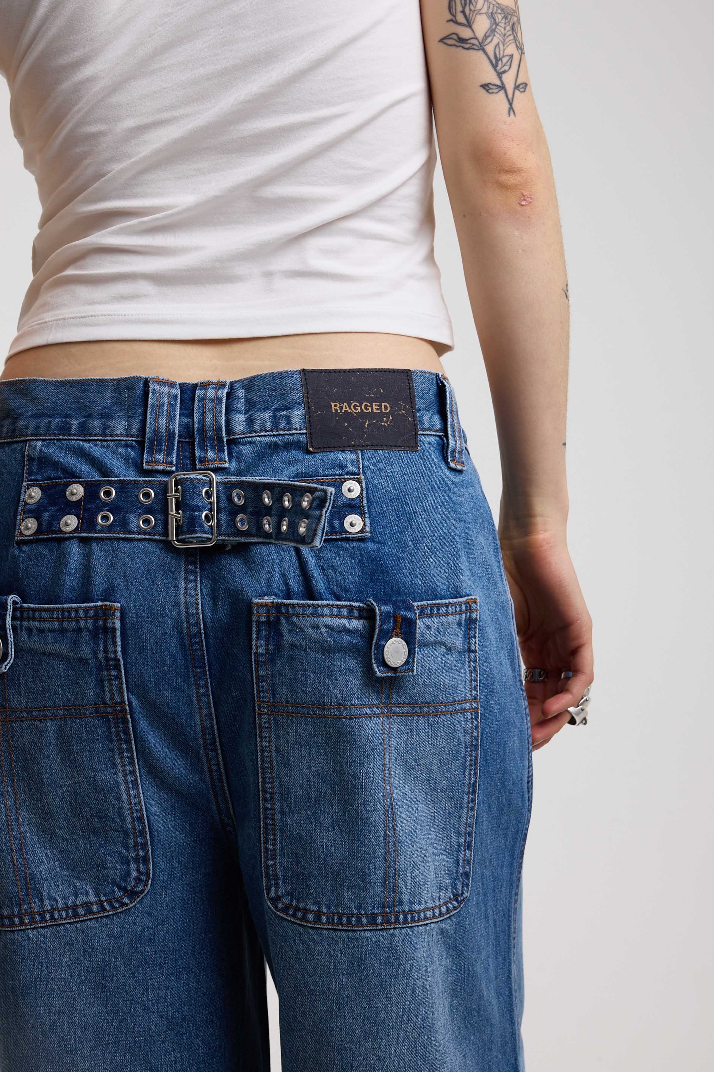 Close up showing hardware eyelet detail cinch back belt on dark blue ultra baggy wide leg jeans, worn by model