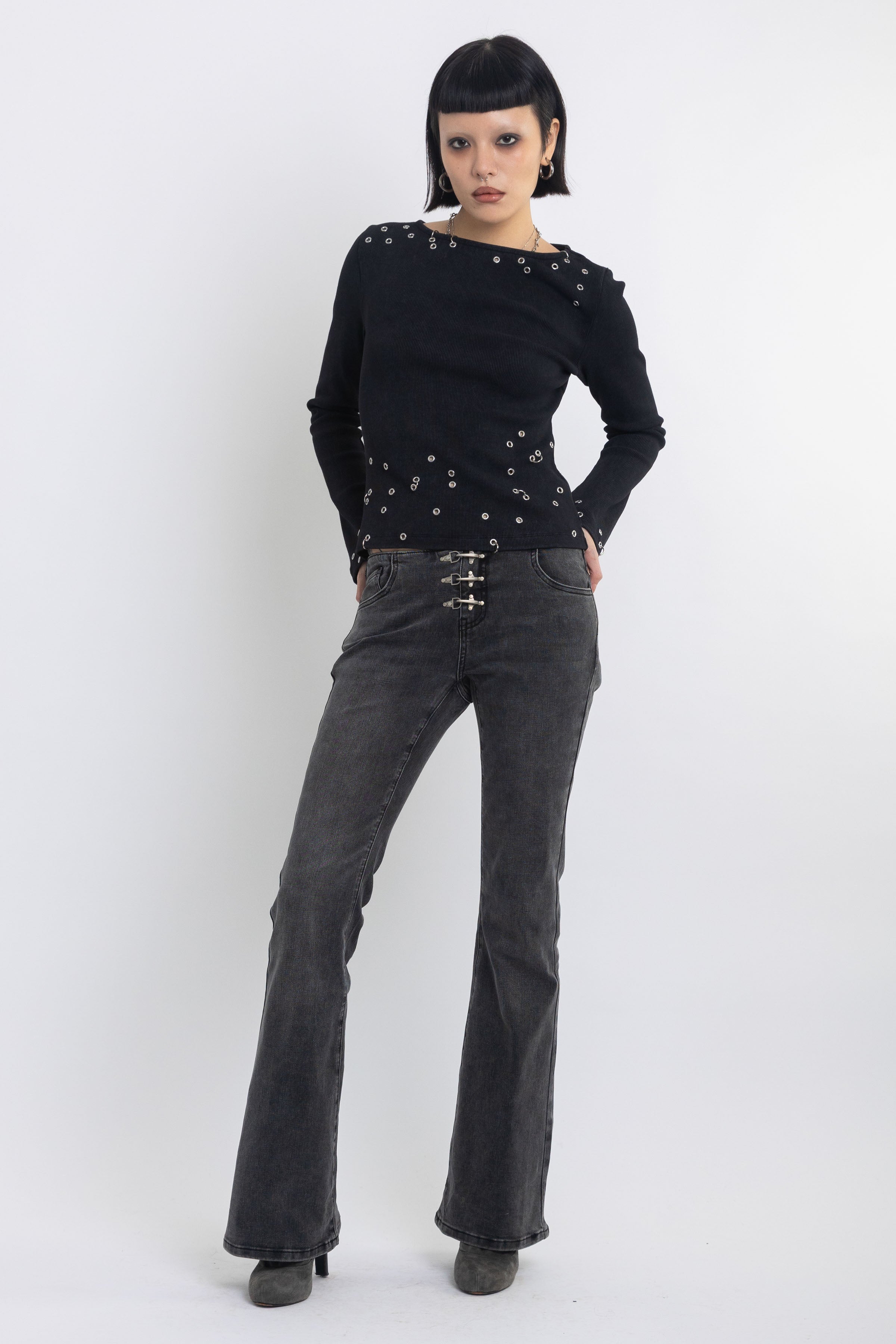 Washed black low rise flare jeans with no waistband and silver clasp hardware, worn by model