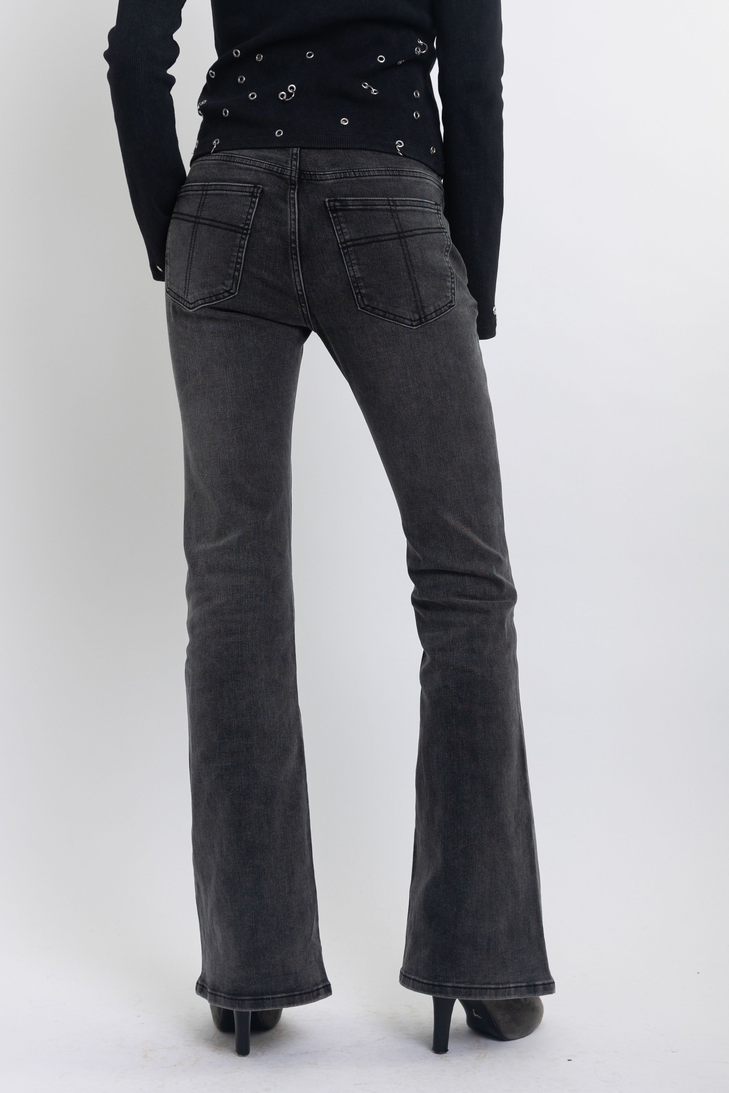 Washed black low rise flare jeans with no waistband and silver clasp hardware, worn by model