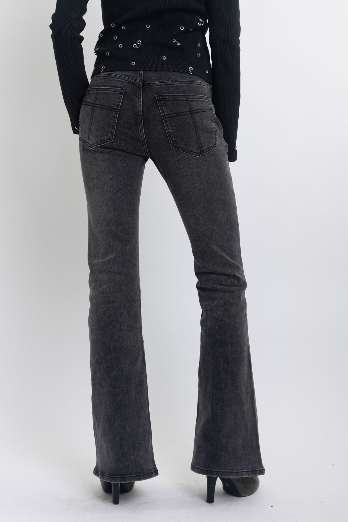 Washed black low rise flare jeans with no waistband and silver clasp hardware, worn by model