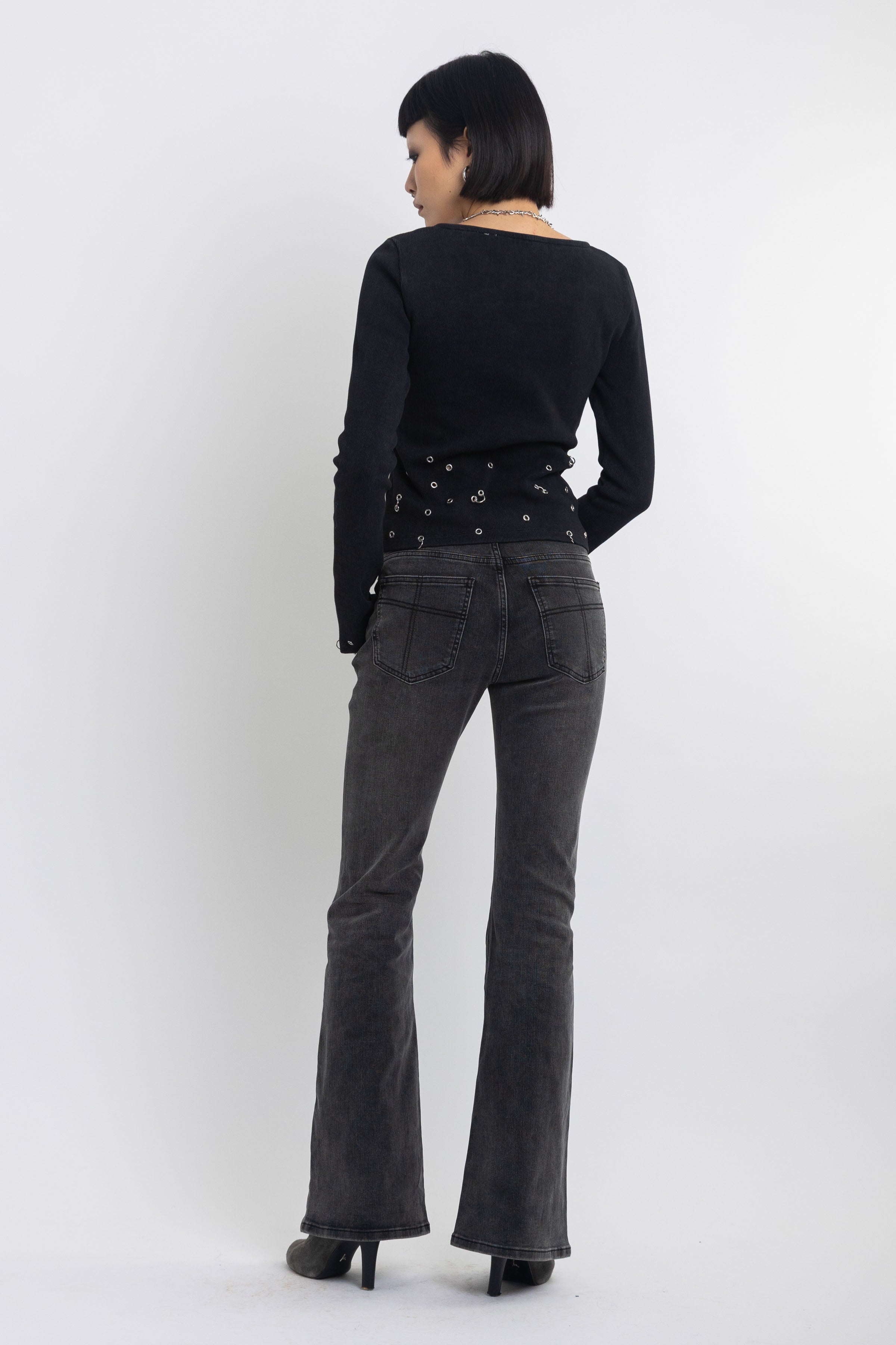 Washed black low rise flare jeans with no waistband and silver clasp hardware, worn by model