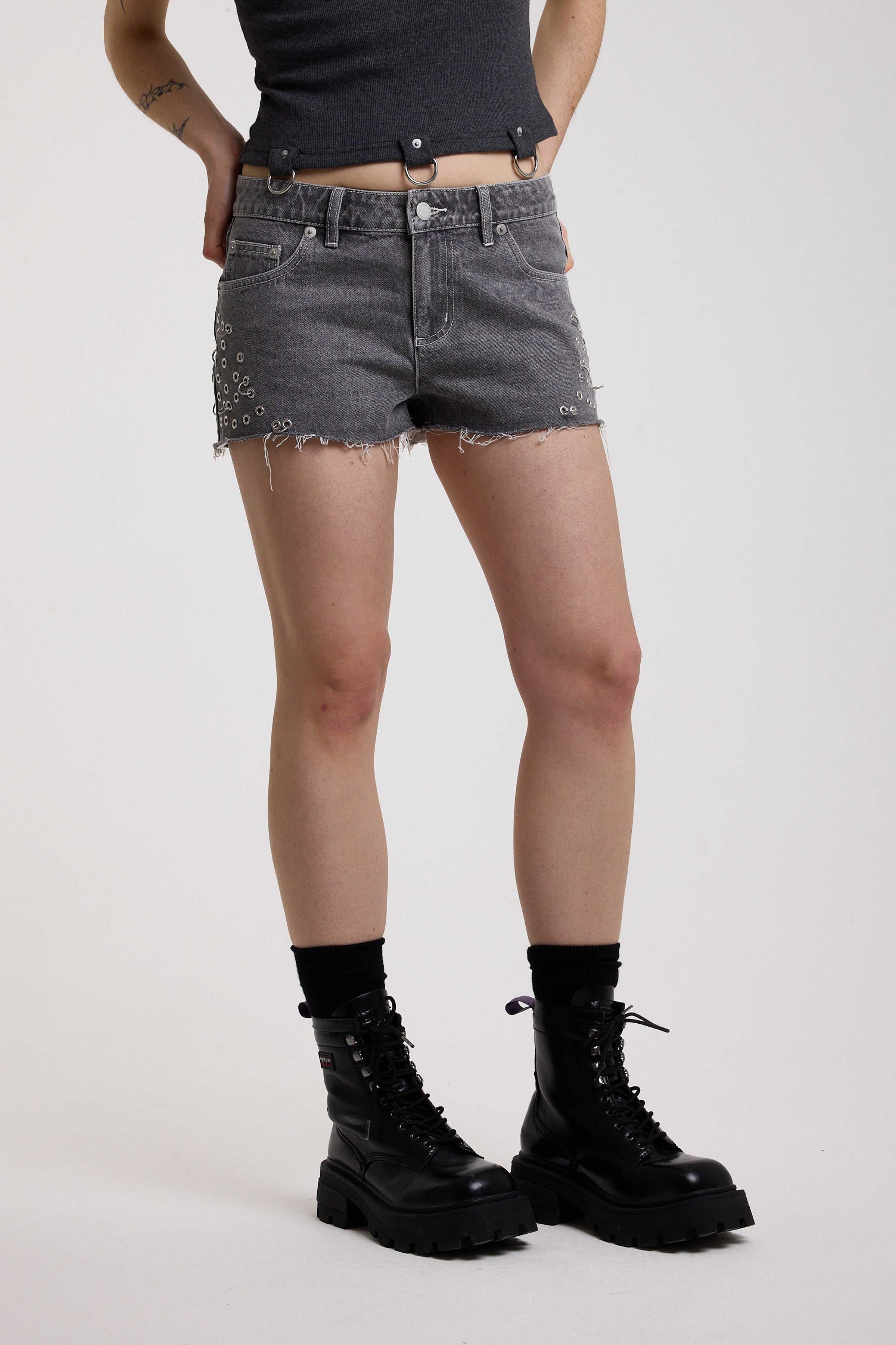 Washed black denim hotpants with silver stud eyelet and piercing hardware, worn by model