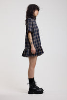 Side image of navy and yellow check shirt style mini dress with peplum hem, worn by model