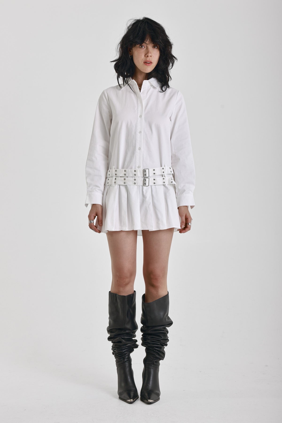 White mini shirt dress with long sleeves, pleated skirt and double eyelet belt, worn by model