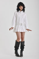 White mini shirt dress with long sleeves, pleated skirt and double eyelet belt, worn by model