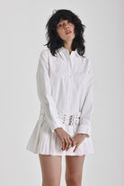 White mini shirt dress with long sleeves, pleated skirt and double eyelet belt, worn by model