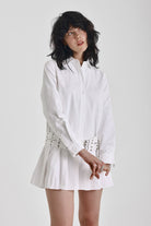 White mini shirt dress with long sleeves, pleated skirt and double eyelet belt, worn by model