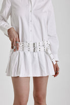 White mini shirt dress with long sleeves, pleated skirt and double eyelet belt, worn by model