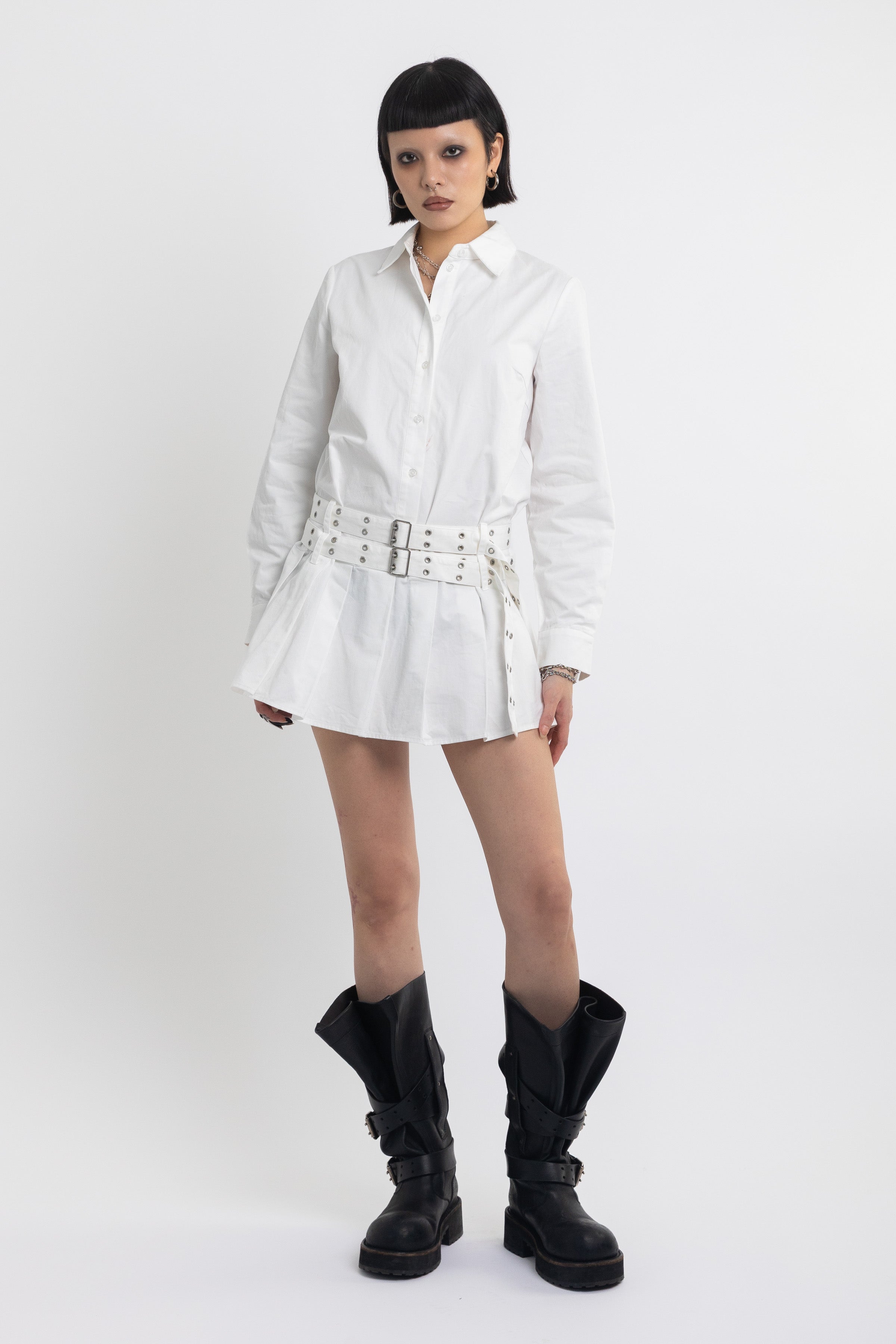 White mini shirt dress with pleated skirt and double eyelet belt, worn by model