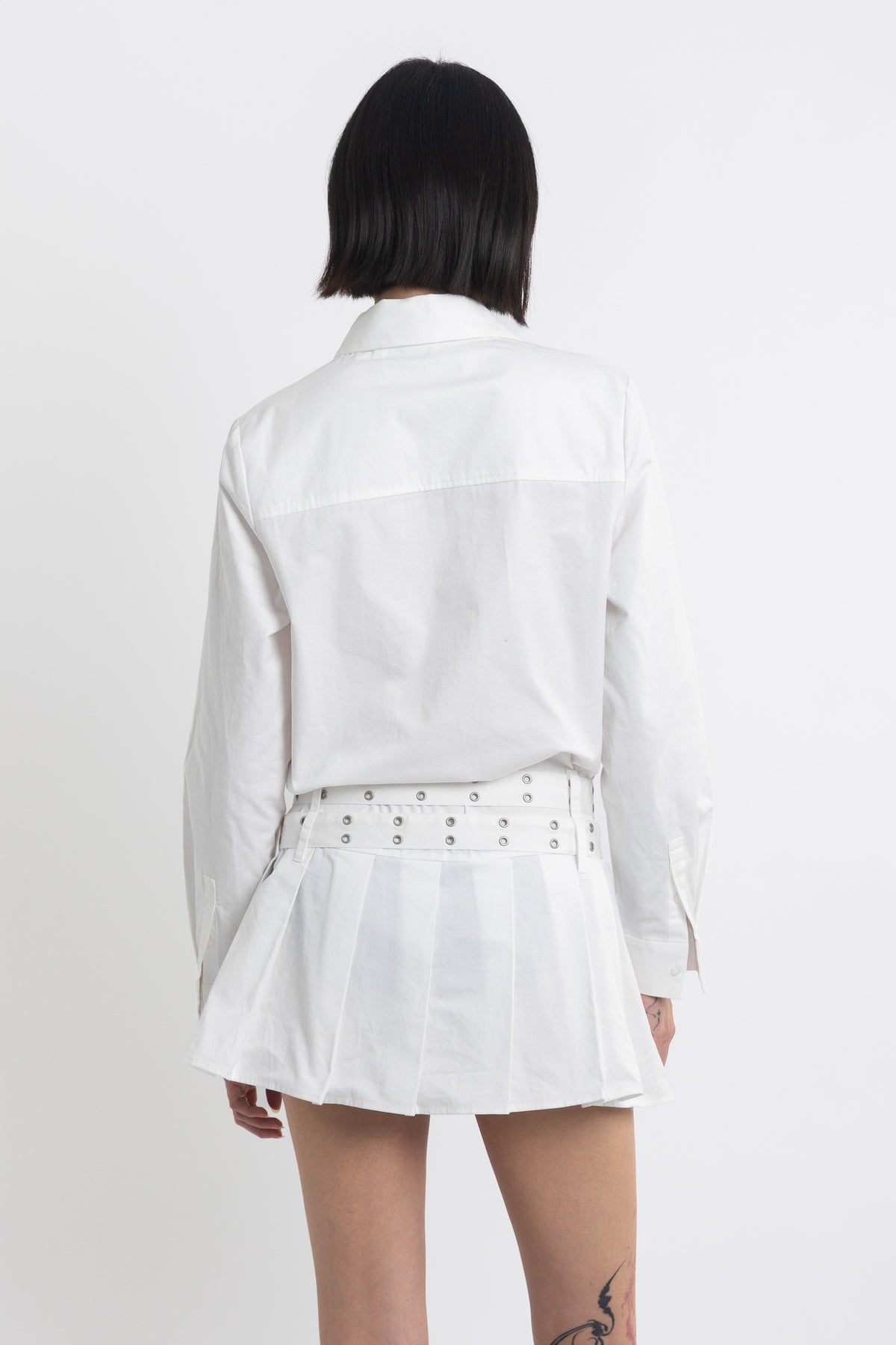 White mini shirt dress with pleated skirt and double eyelet belt, worn by model