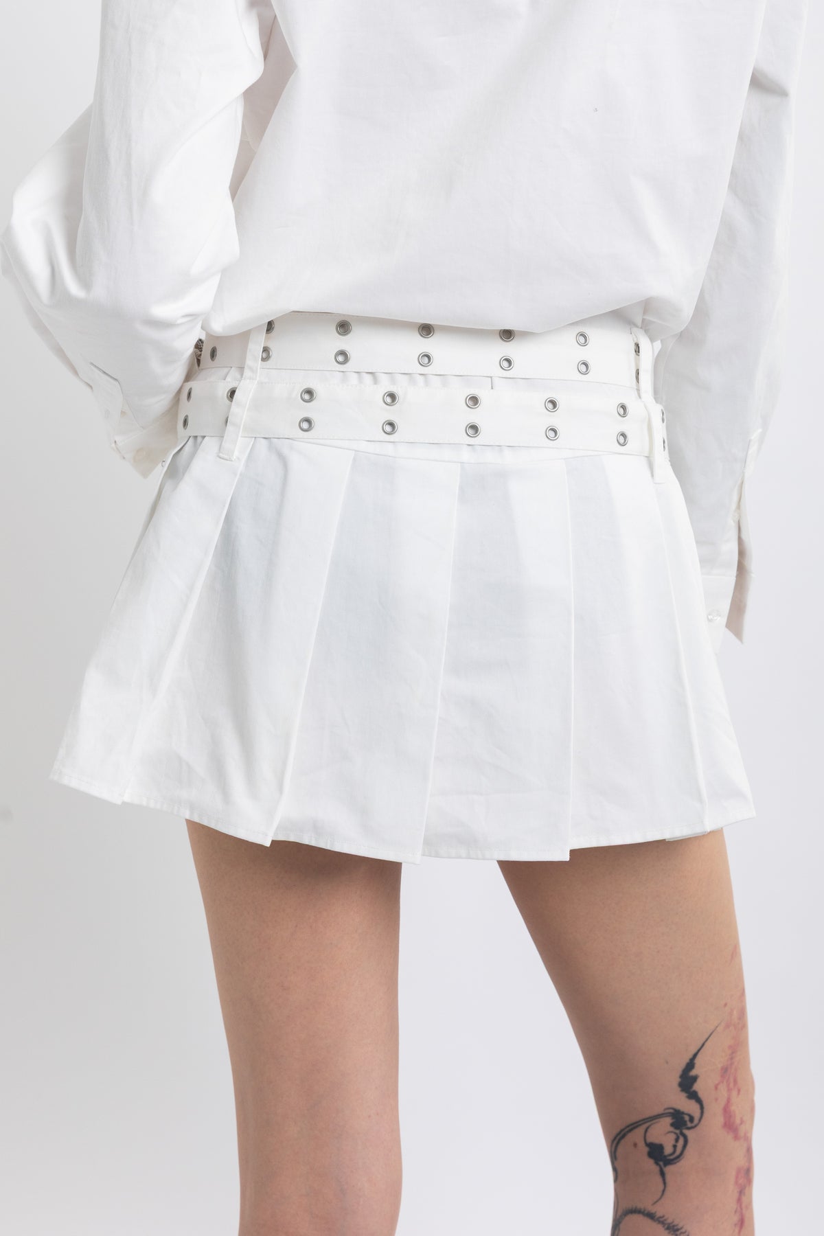 White mini shirt dress with pleated skirt and double eyelet belt, worn by model