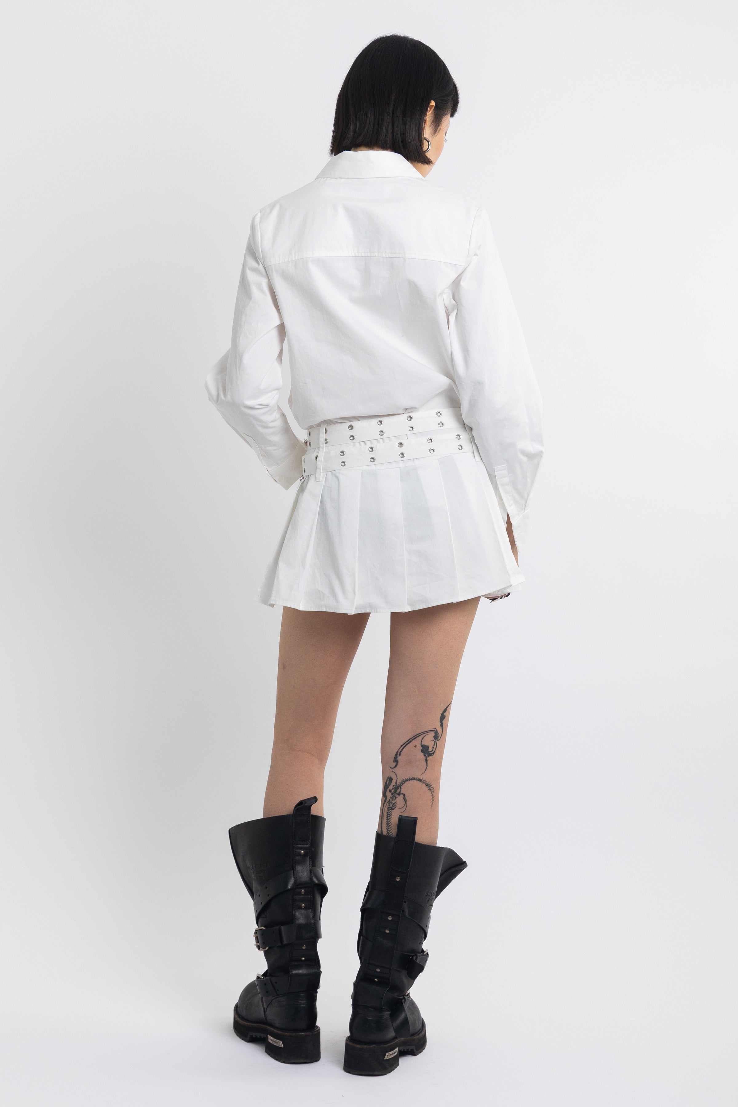 White mini shirt dress with pleated skirt and double eyelet belt, worn by model