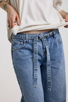 Close up of denim tie D-ring belt on blue baggy balloon boyfriend jeans, worn by model
