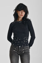 Black ribbed long sleeve top with piercing and stud hardware details, worn by a model