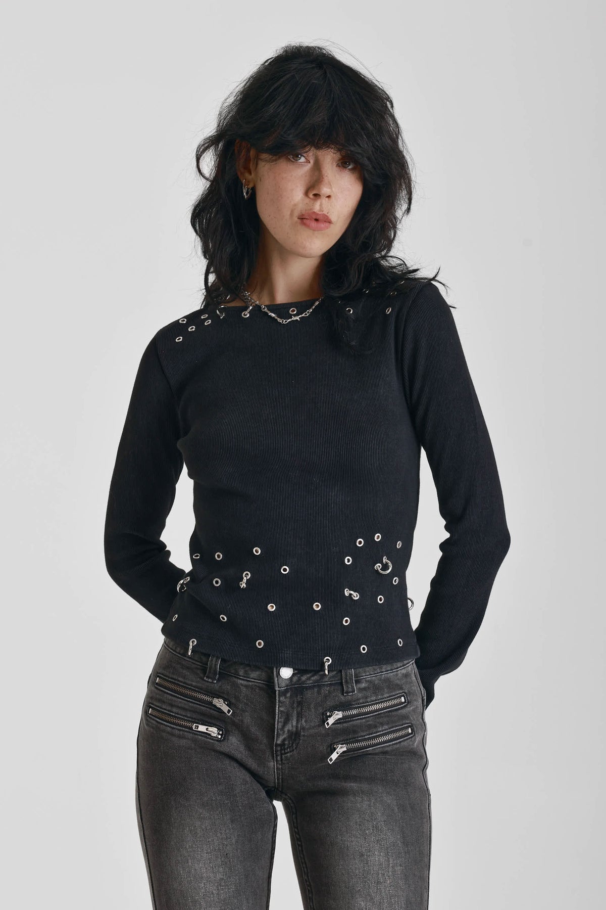 Black ribbed long sleeve top with piercing and stud hardware details, worn by a model