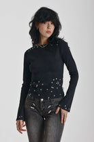 Black ribbed long sleeve top with piercing and stud hardware details, worn by a model
