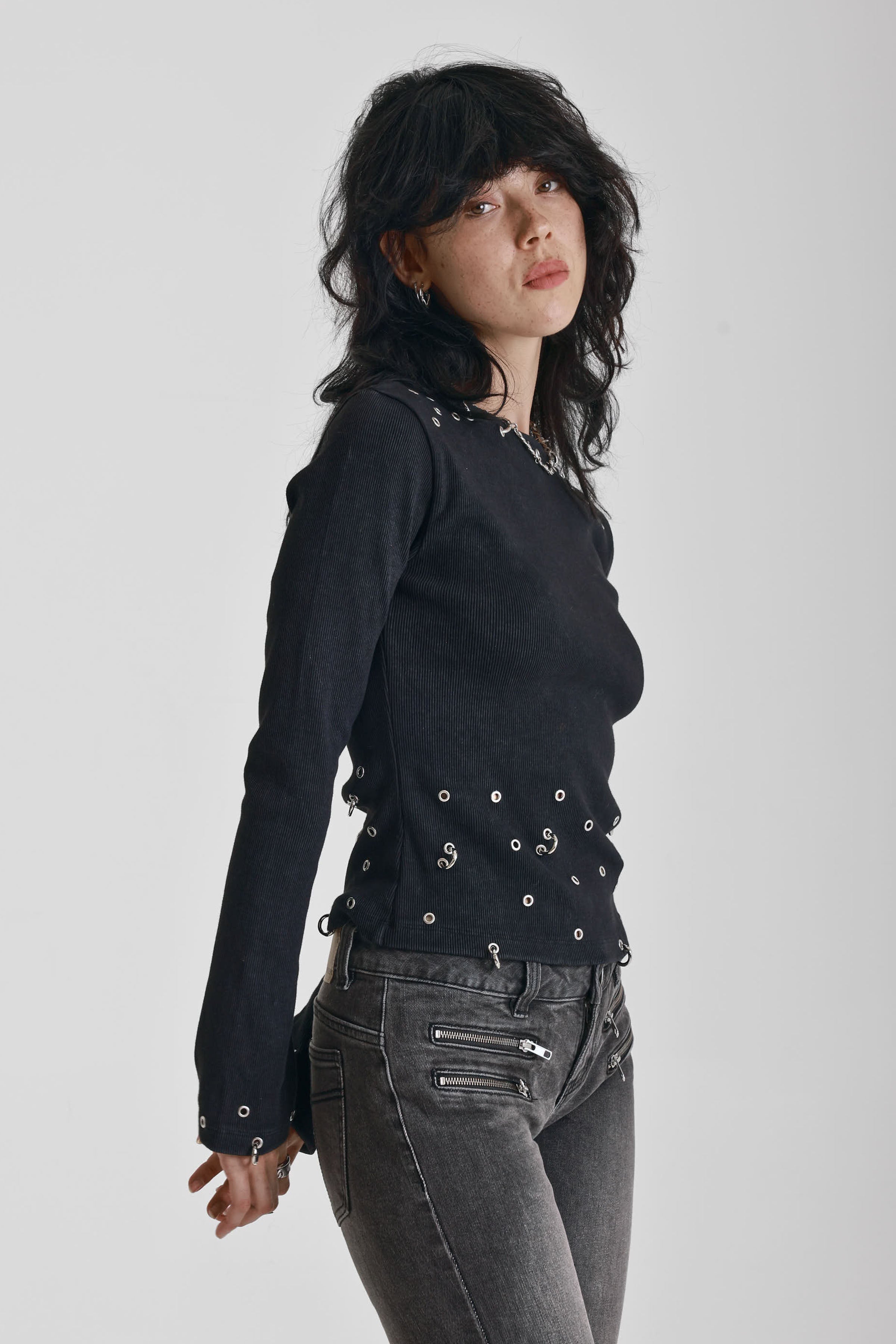 Black ribbed long sleeve top with piercing and stud hardware details, worn by a model