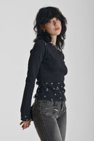 Black ribbed long sleeve top with piercing and stud hardware details, worn by a model