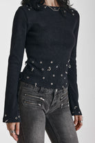 Black ribbed long sleeve top with piercing and stud hardware details, worn by a model