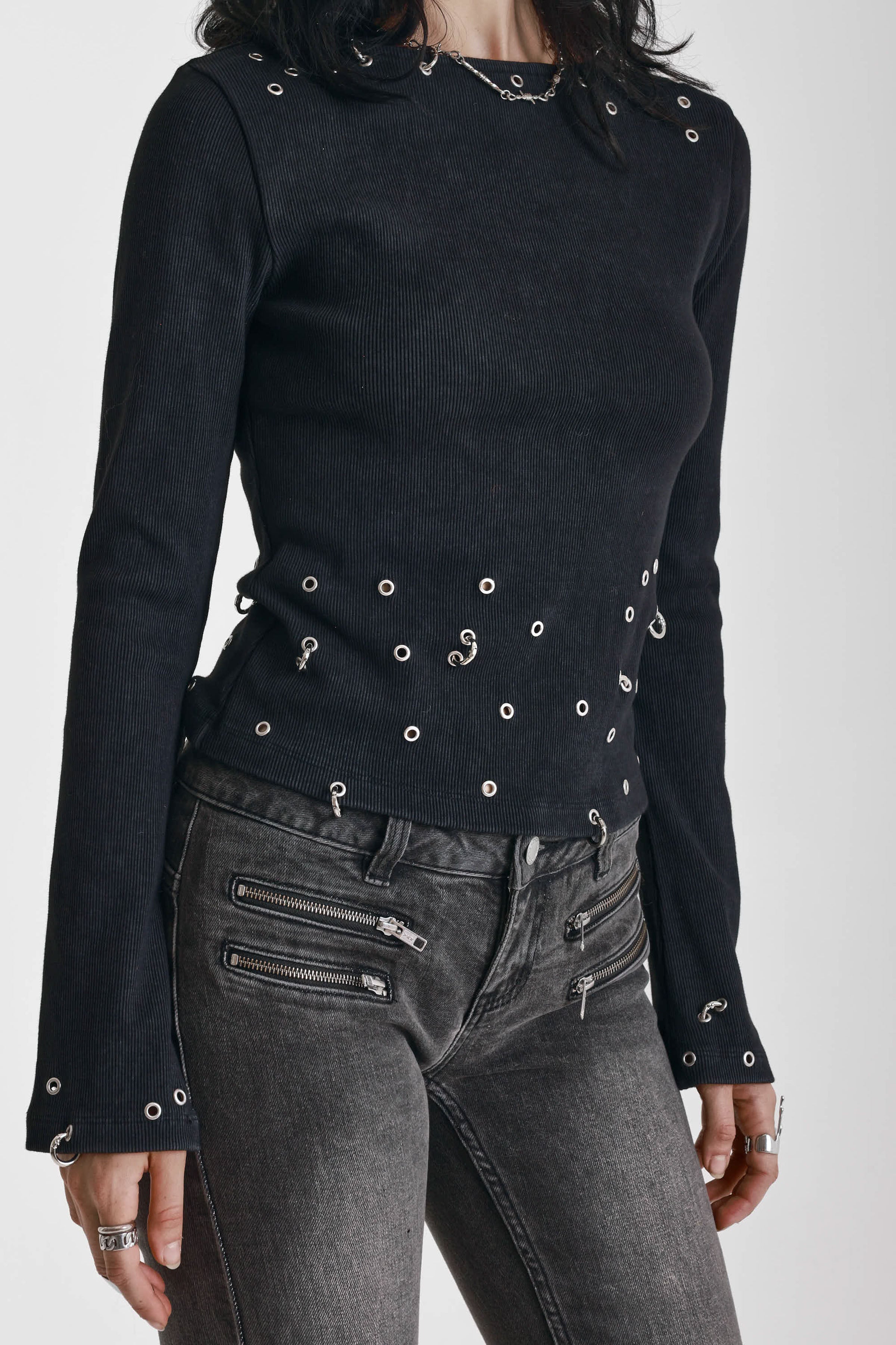 Black ribbed long sleeve top with piercing and stud hardware details, worn by a model