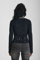 Black ribbed long sleeve top with piercing and stud hardware details, worn by a model