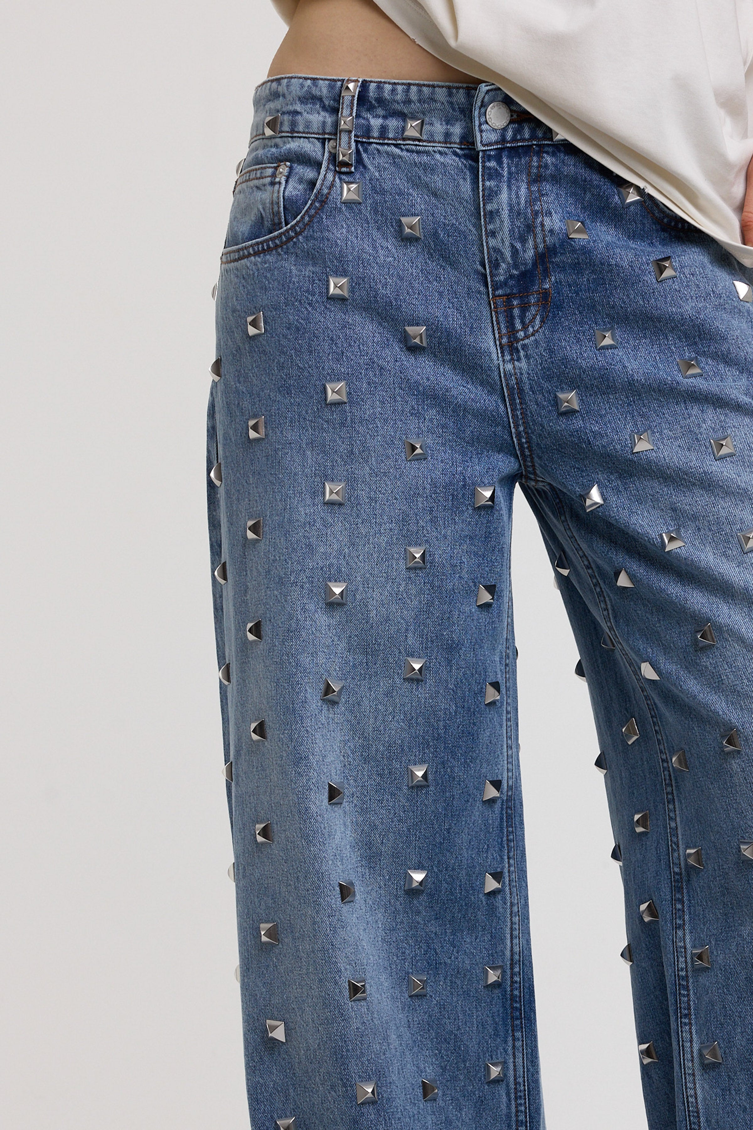 Close up of silver hardware stud detail on blue baggy release jeans, worn by model