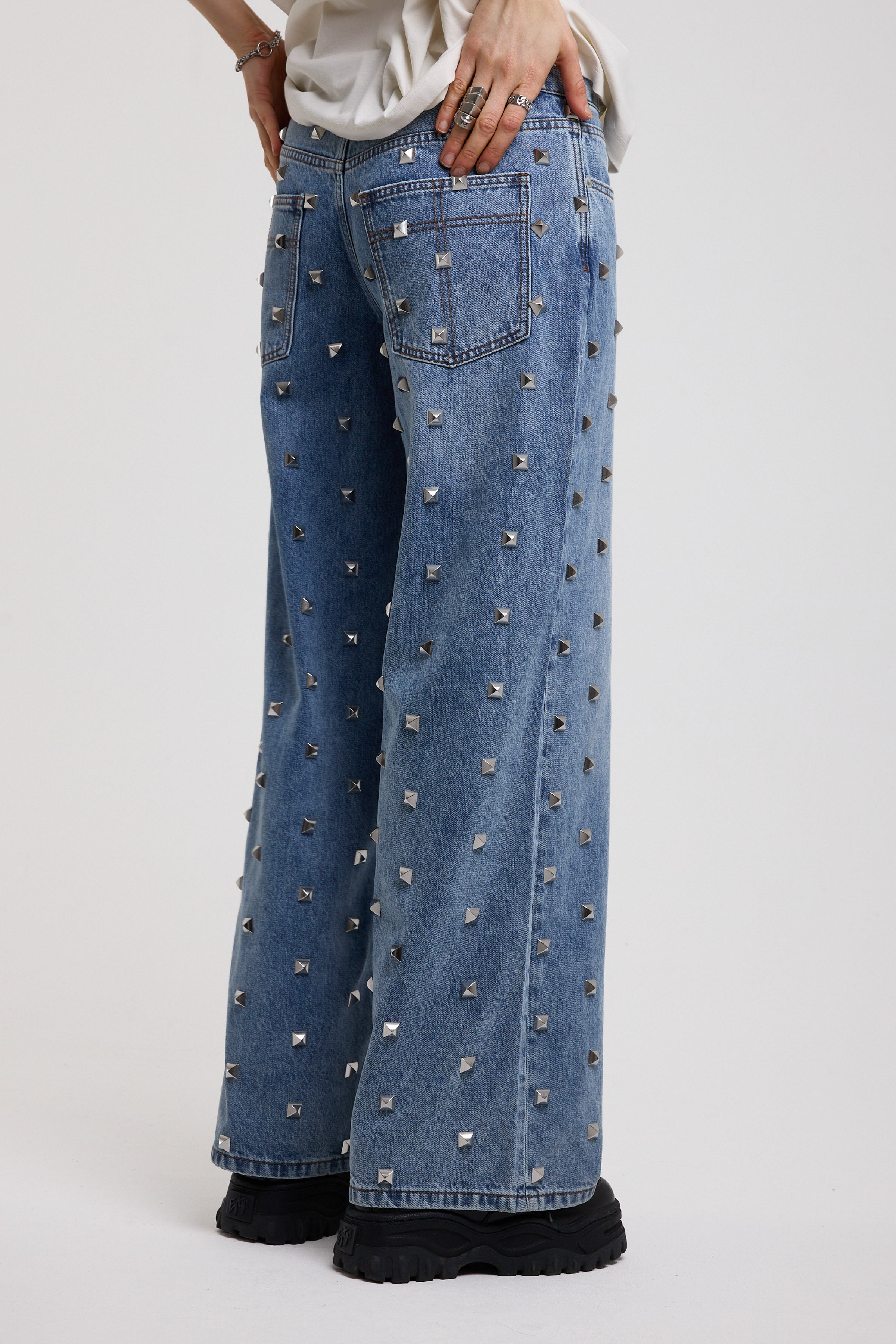 Back image of blue baggy release jeans with silver stud detail, worn by model 
