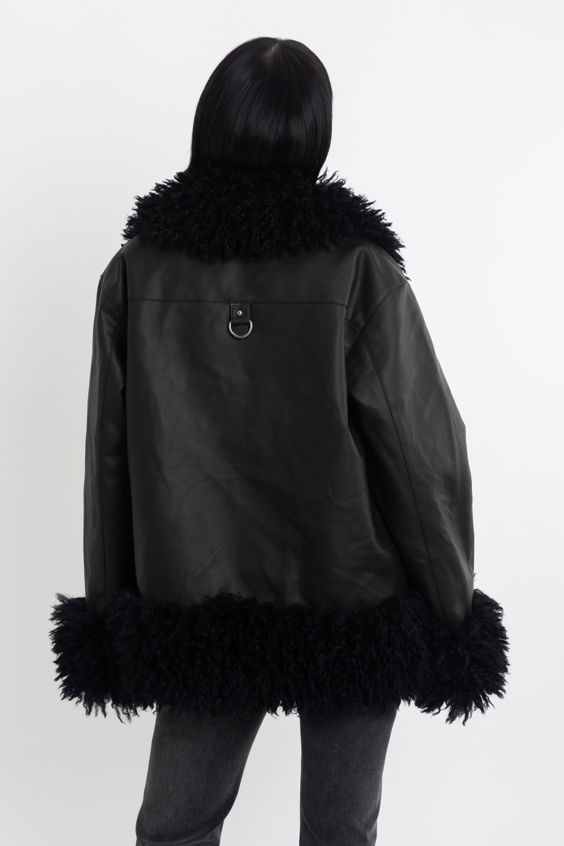 Black faux leather biker jacket with oversized shearling trims and silver hardware, worn by model