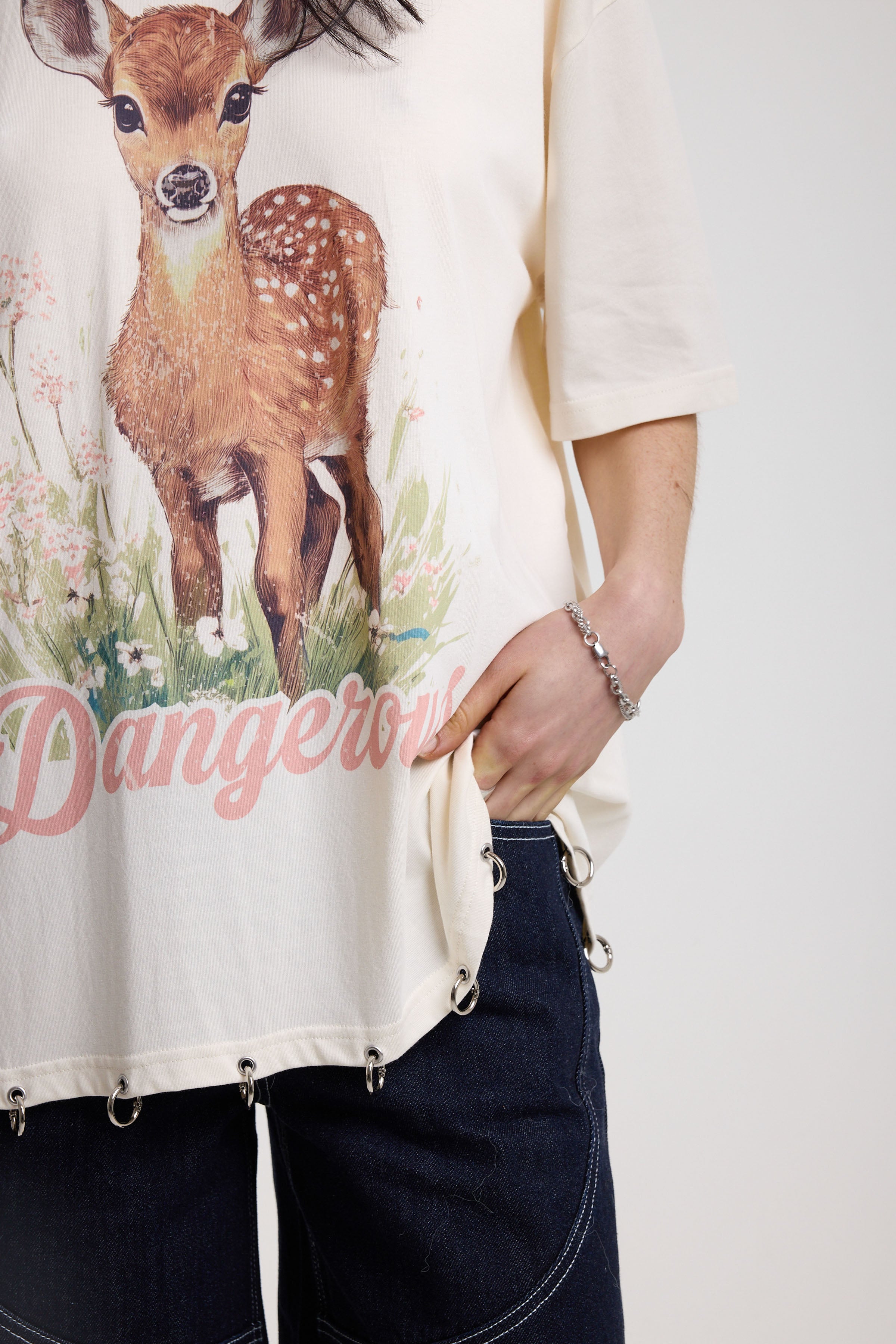 Close up of off-white oversized t-shirt with graphic deer print and silver O-ring hardware detail, worn by model