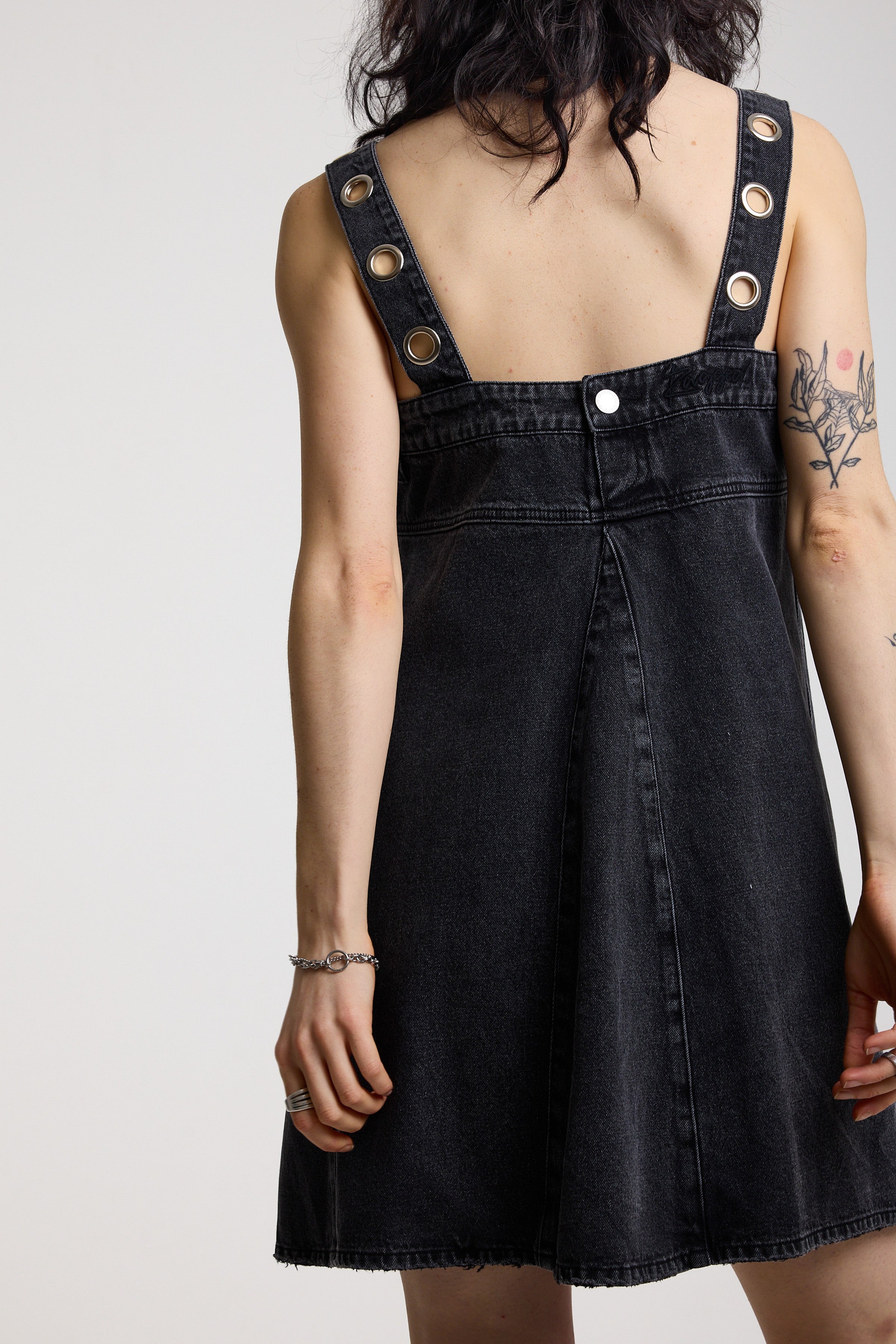Back image of washed black denim square neck mini dress with eyelet detail straps, worn by model