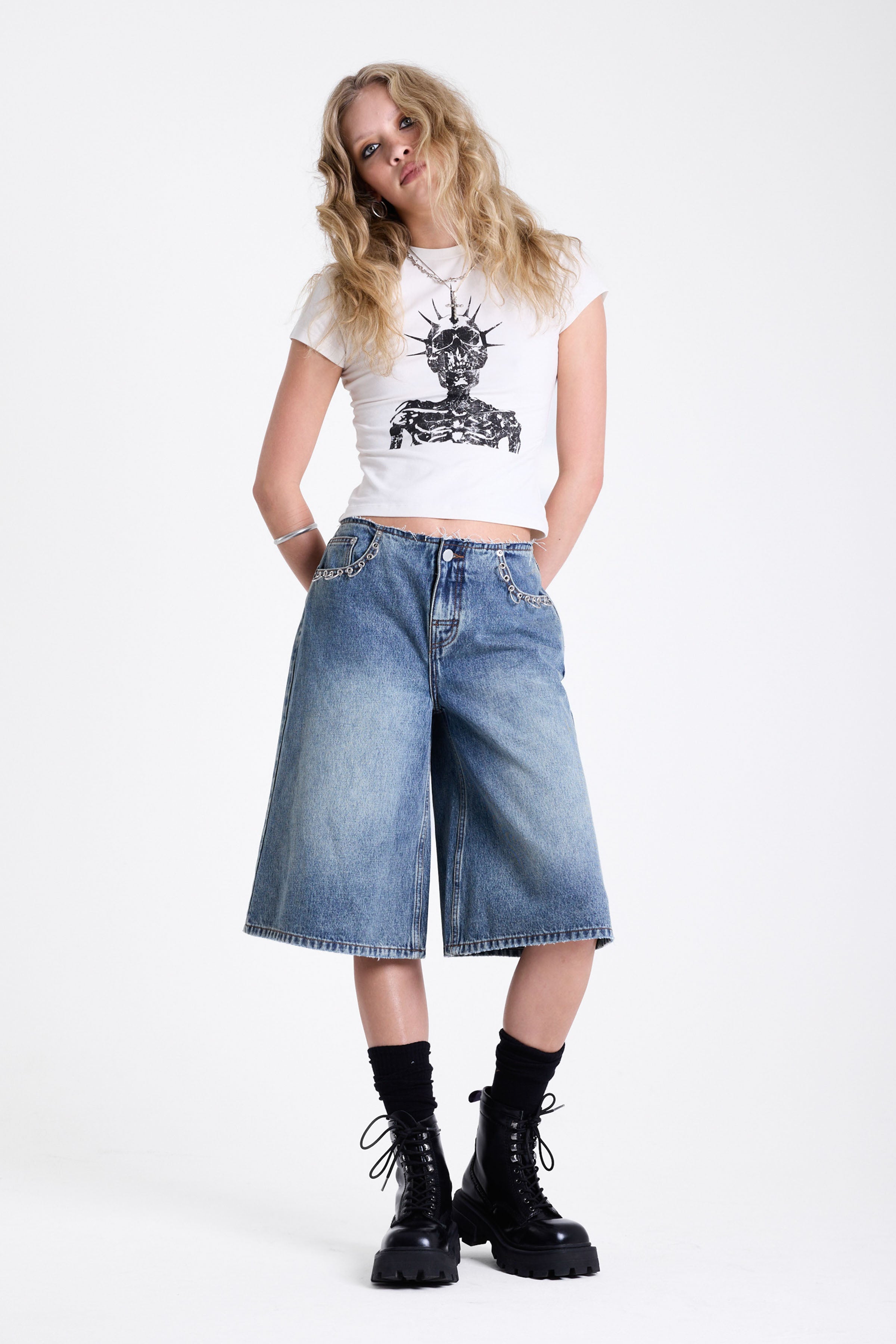 Mid blue denim longline jorts with no waistband and silver piercing hardware detail, worn by model