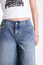 Mid blue denim longline jorts with no waistband and silver piercing hardware detail, worn by model