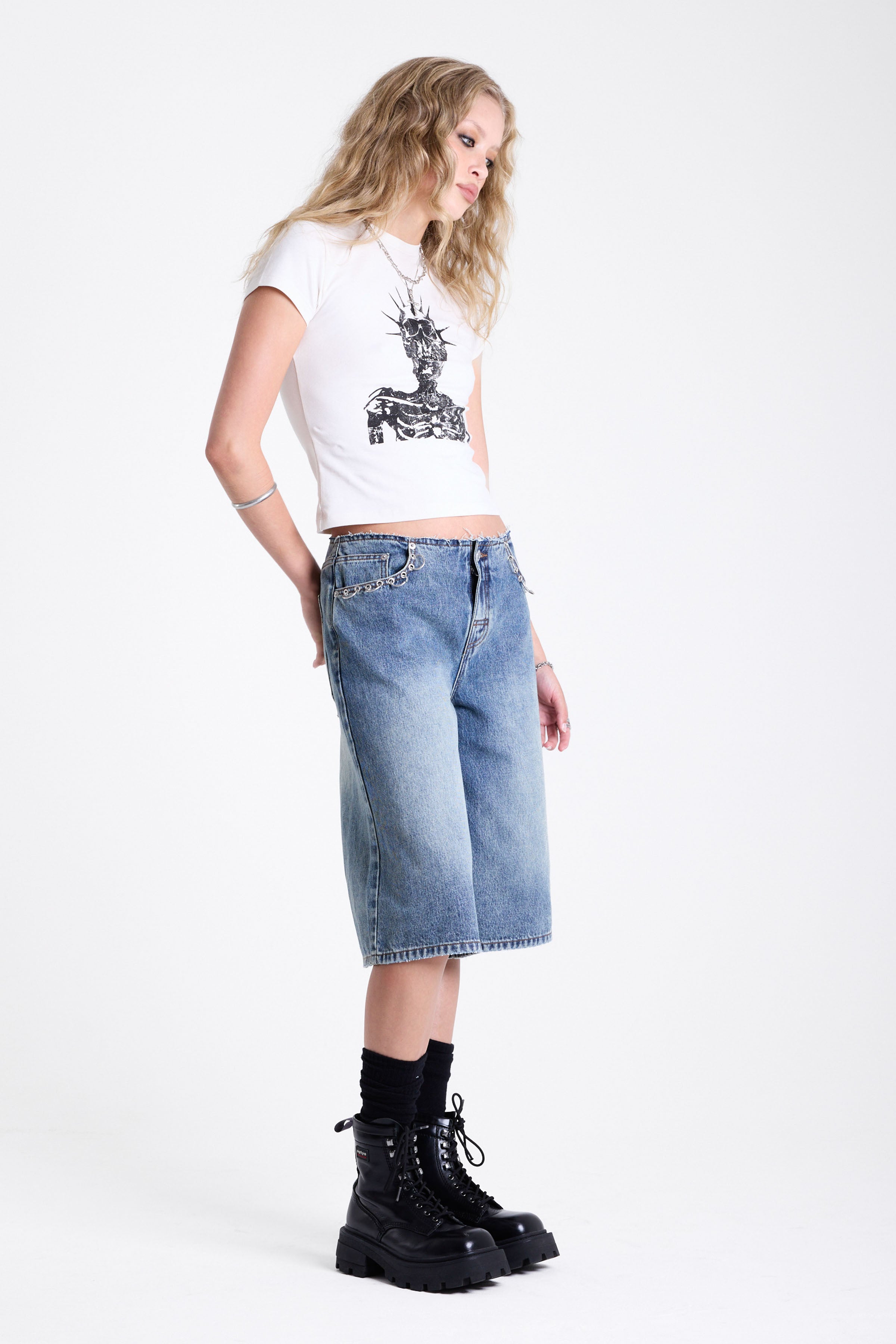 Mid blue denim longline jorts with no waistband and silver piercing hardware detail, worn by model